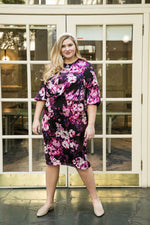 Load image into Gallery viewer, Tall blonde size 18 woman wears a straight dress with a draped top, and cross pleated top and billow sleeves. The print is purple and white flowers with a black background  
